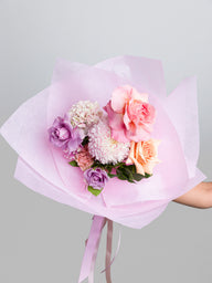 A bouquet of pastel colored roses, disbuds, and carnations wrapped in pink paper with a ribbon.
