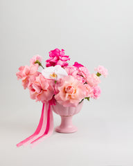 A bouquet of pink roses, orchids, and carnations arranged in a pink vase with a ribbon.