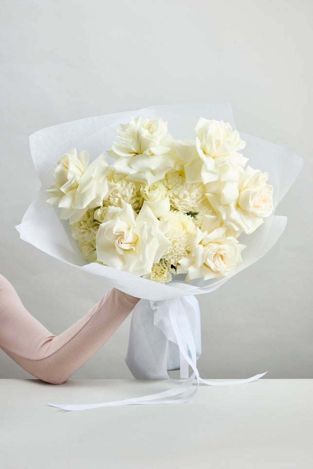 Pure grace white bouquet flowers held by a person against a plain background by flowerdose.