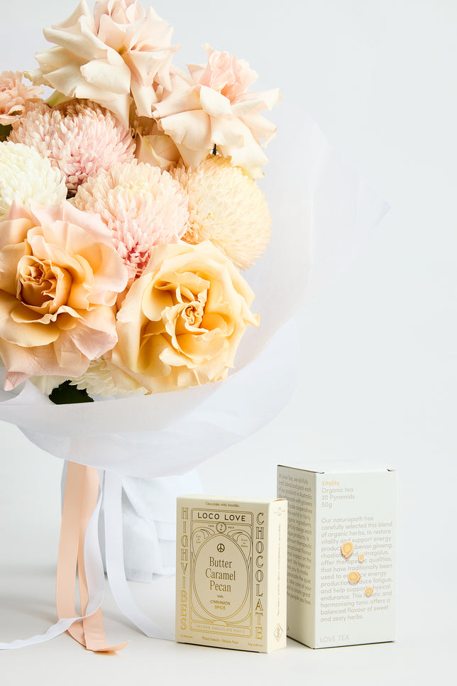 Spring Fling Gift Set by Flowerdose — a joyful pastel bouquet featuring peach roses, blush chrysanthemums, and creamy disbuds, wrapped in crisp white paper with satin ribbons. Paired with Loco Love Butter Caramel Pecan chocolate and Vitality organic tea, this luxury Melbourne florist gift is perfect for birthdays, thank-you gestures, and everyday celebrations.